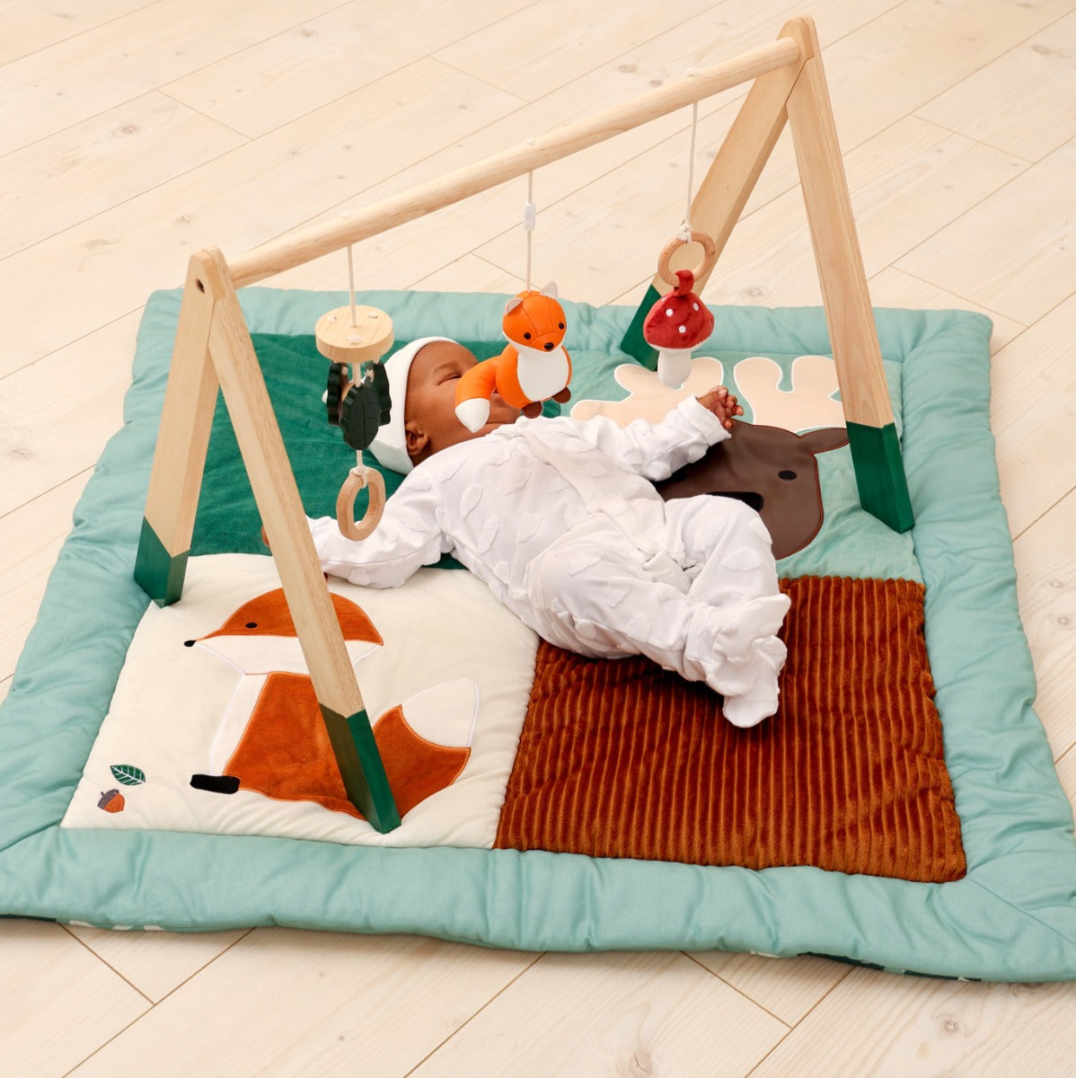 Baby lying on Little Big Friends Patchwork kids reversible playmat and playing with wooden activity gym