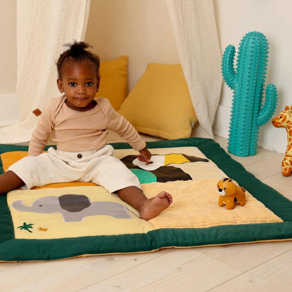 Baby sitting on Little Big Friends Patchwork kids reversible playmat and playing with tiny tiger, giraffe