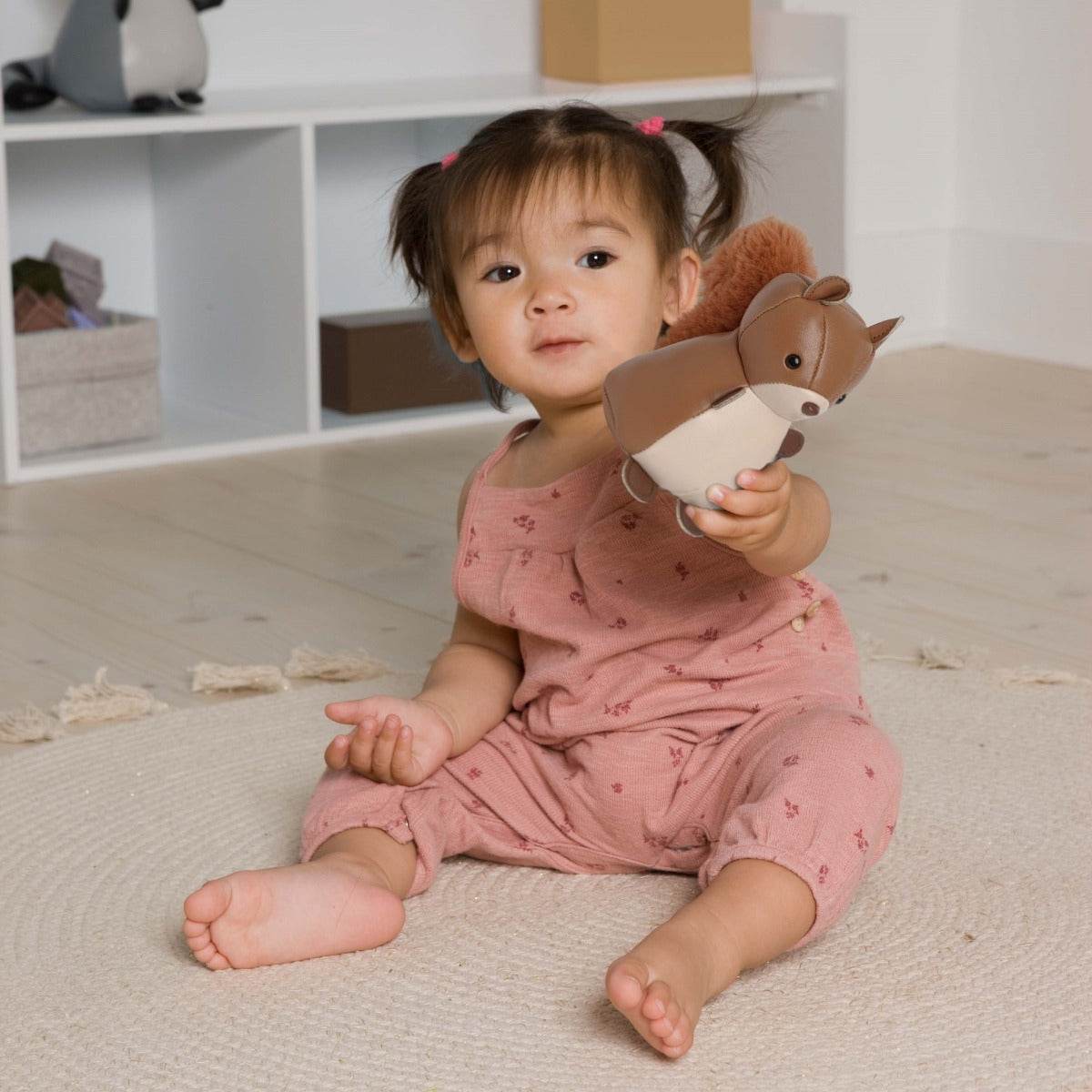 Baby girl holding Tiny Squirrel Toy from Little Big Friends sitting on the floor