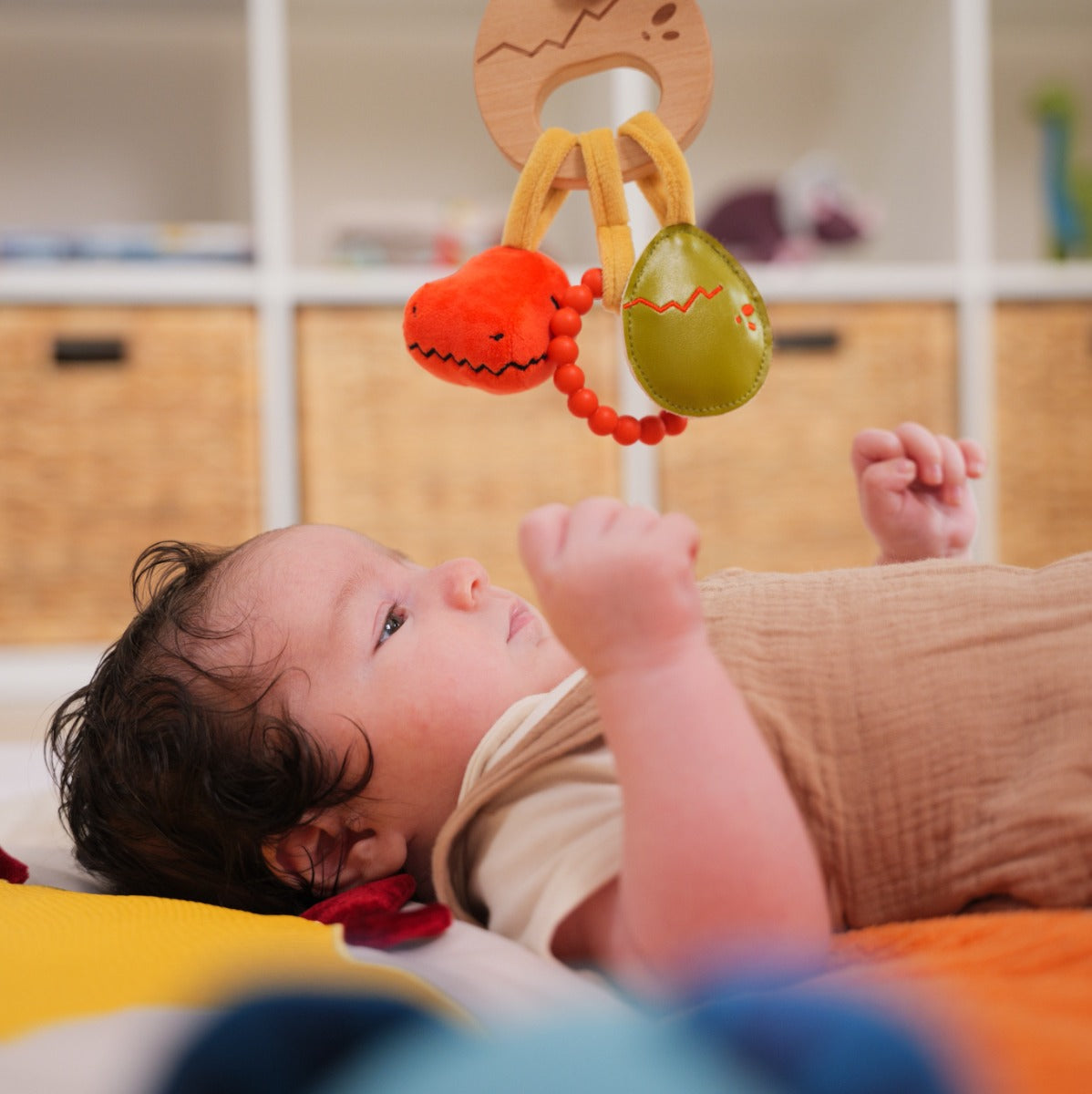 Baby playing with hanging Little big friends wooden rattle with dino theme