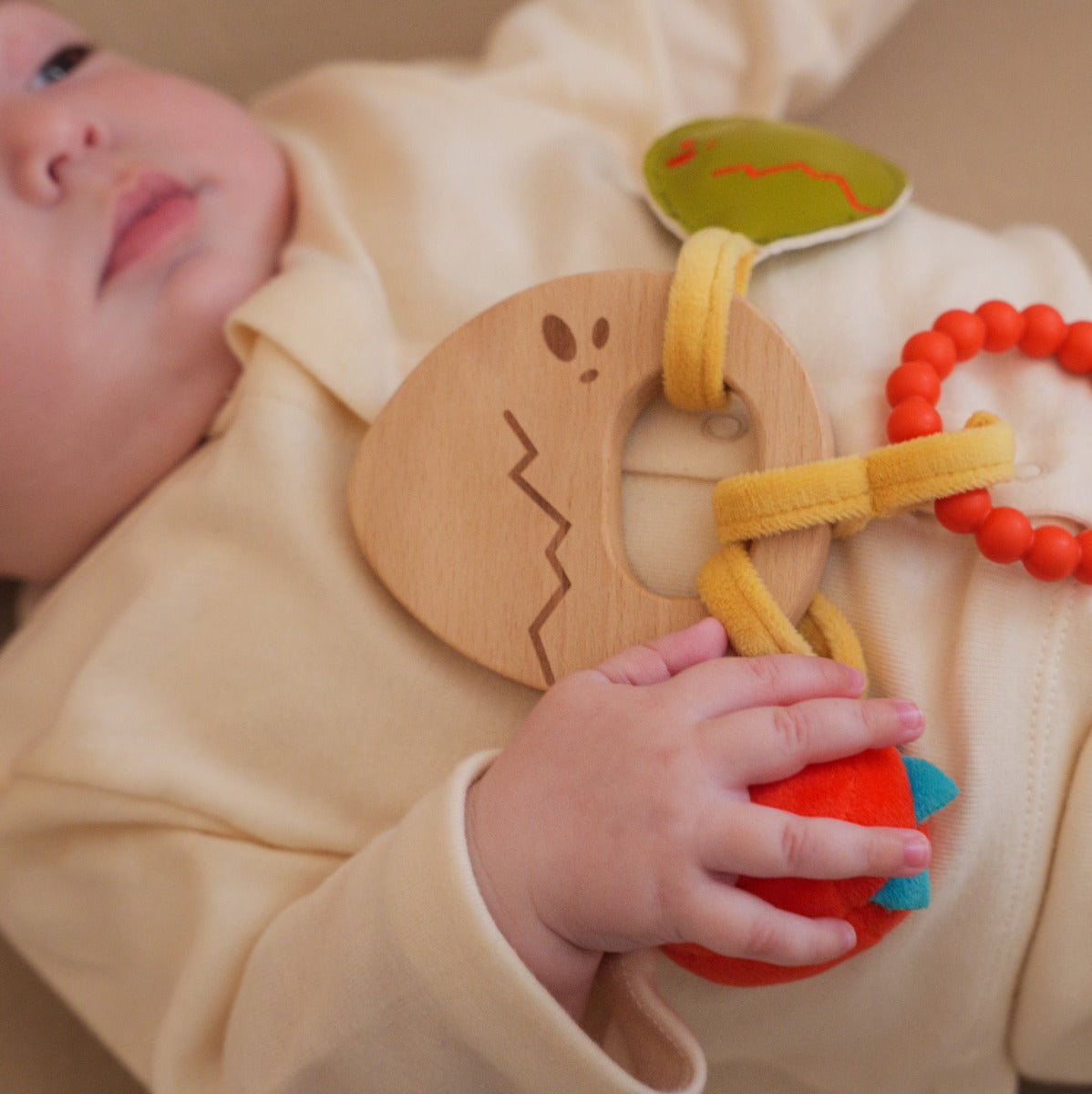Baby holding Little big friends wooden rattle with dino theme