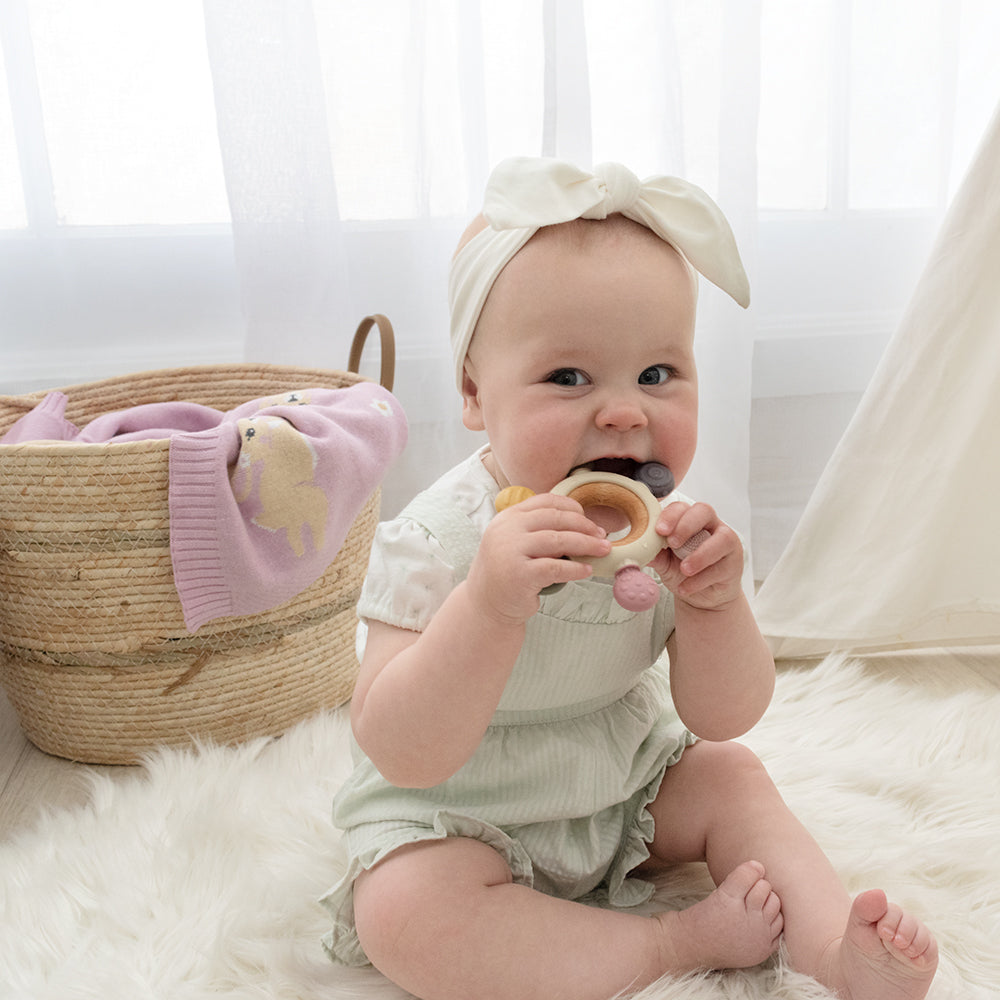 Baby girl with Multi-surface teething wheel from Playground in rose in her mouth