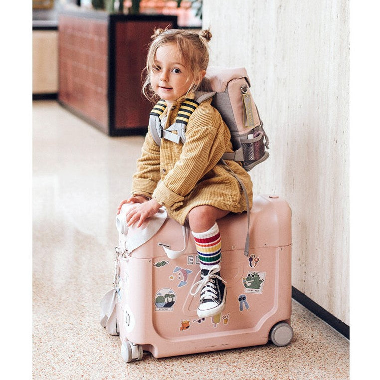 Child sitting on Bedbox while wearing JetKids™ by Stokke® Crew Backpack in Pink Lemonade