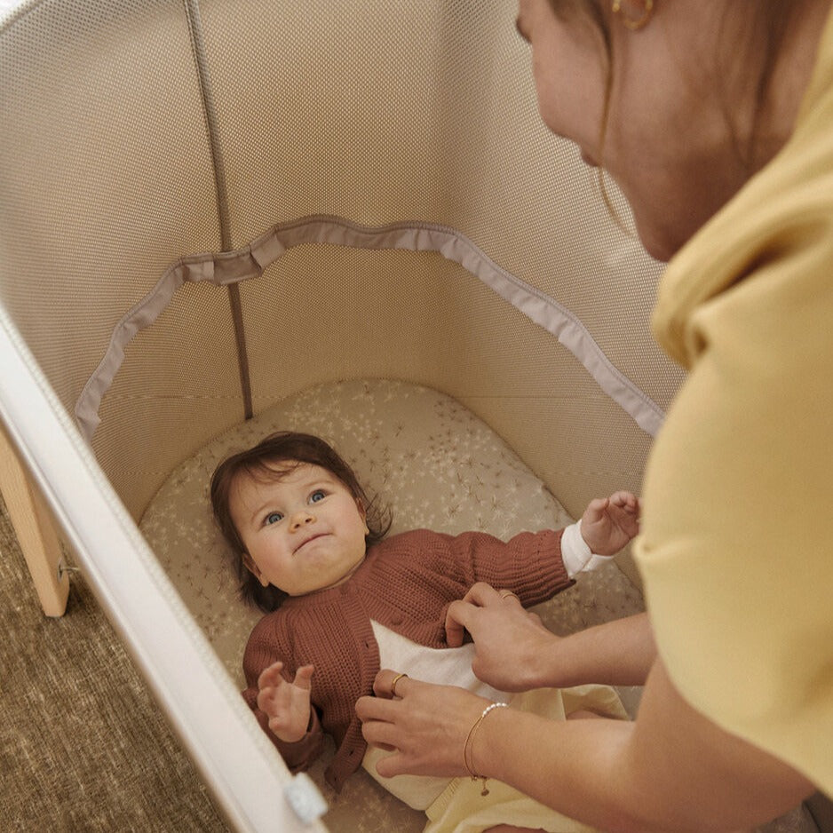 Baby sleeping in extended Snoozi baby portable bassinet from Stokke