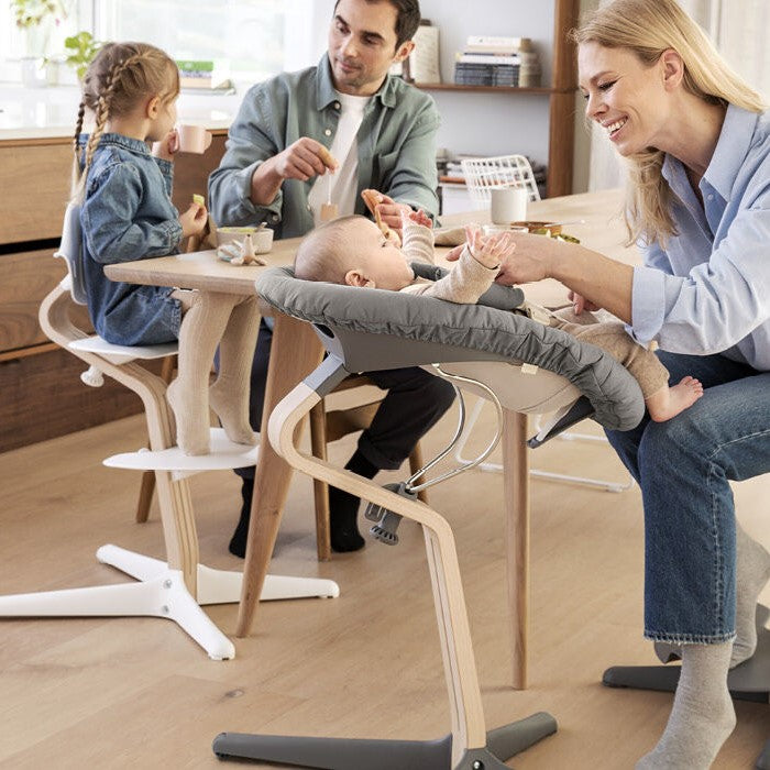 Nomi Natural Gray and white highchair from Stokke with kids and parents in dinning area.