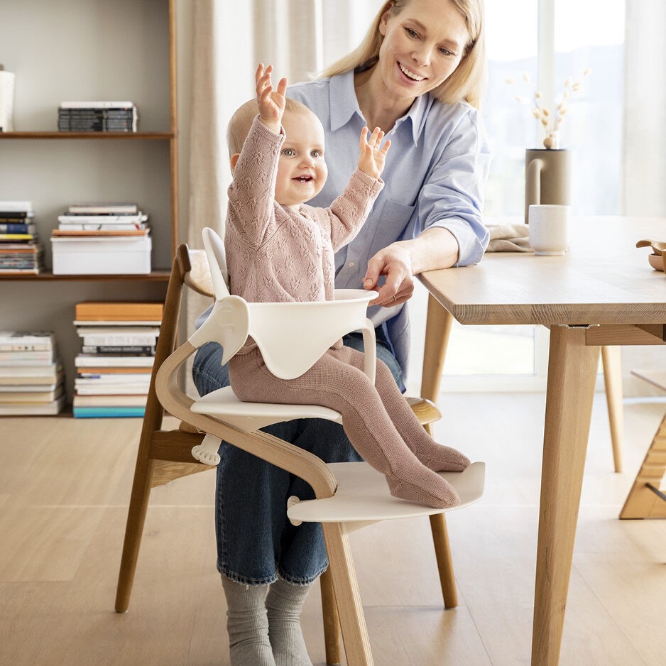 mother watching Baby girl happily sitting in Nomi Babyset in White from Stokke at dinner table