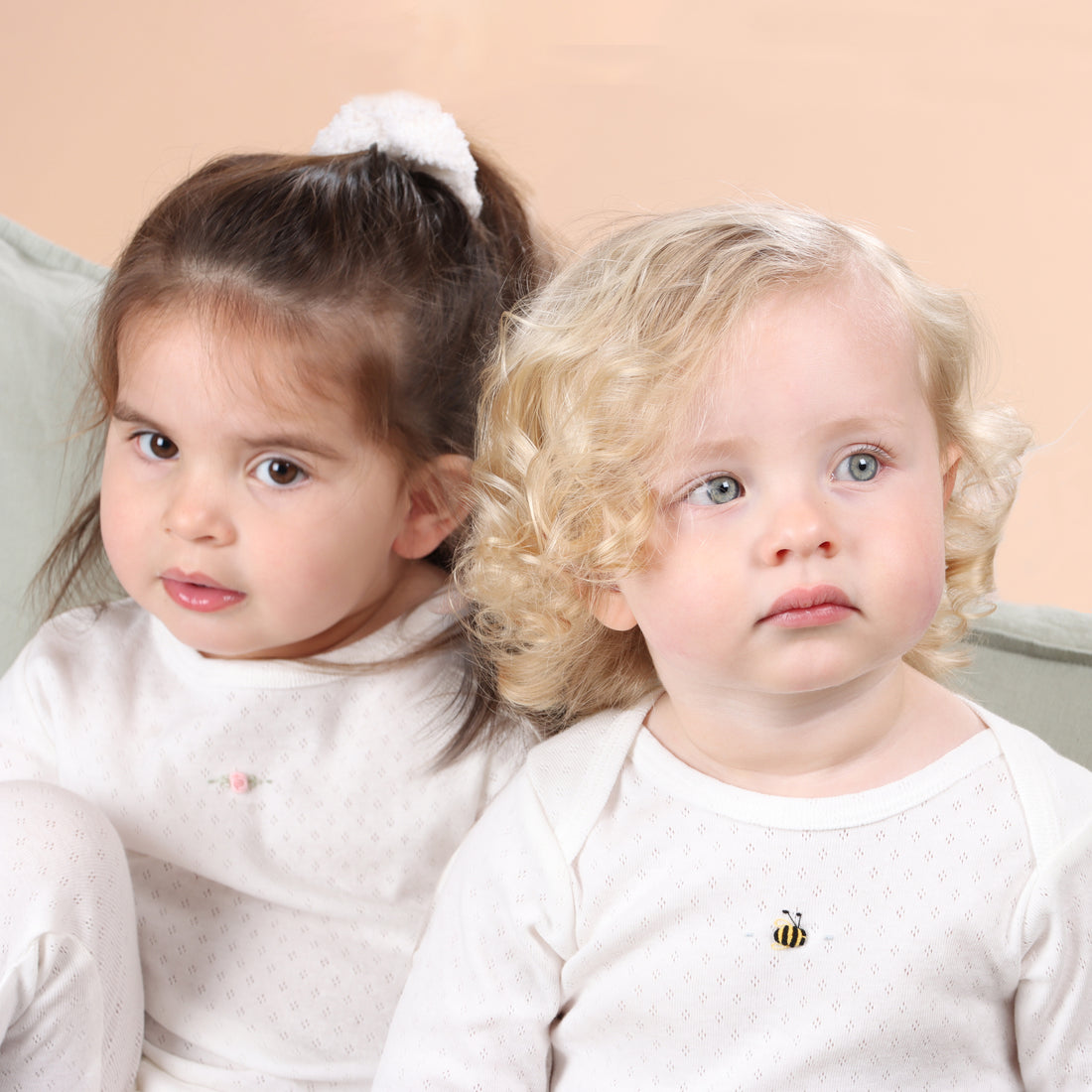 Two young children sitting close together against a beige background