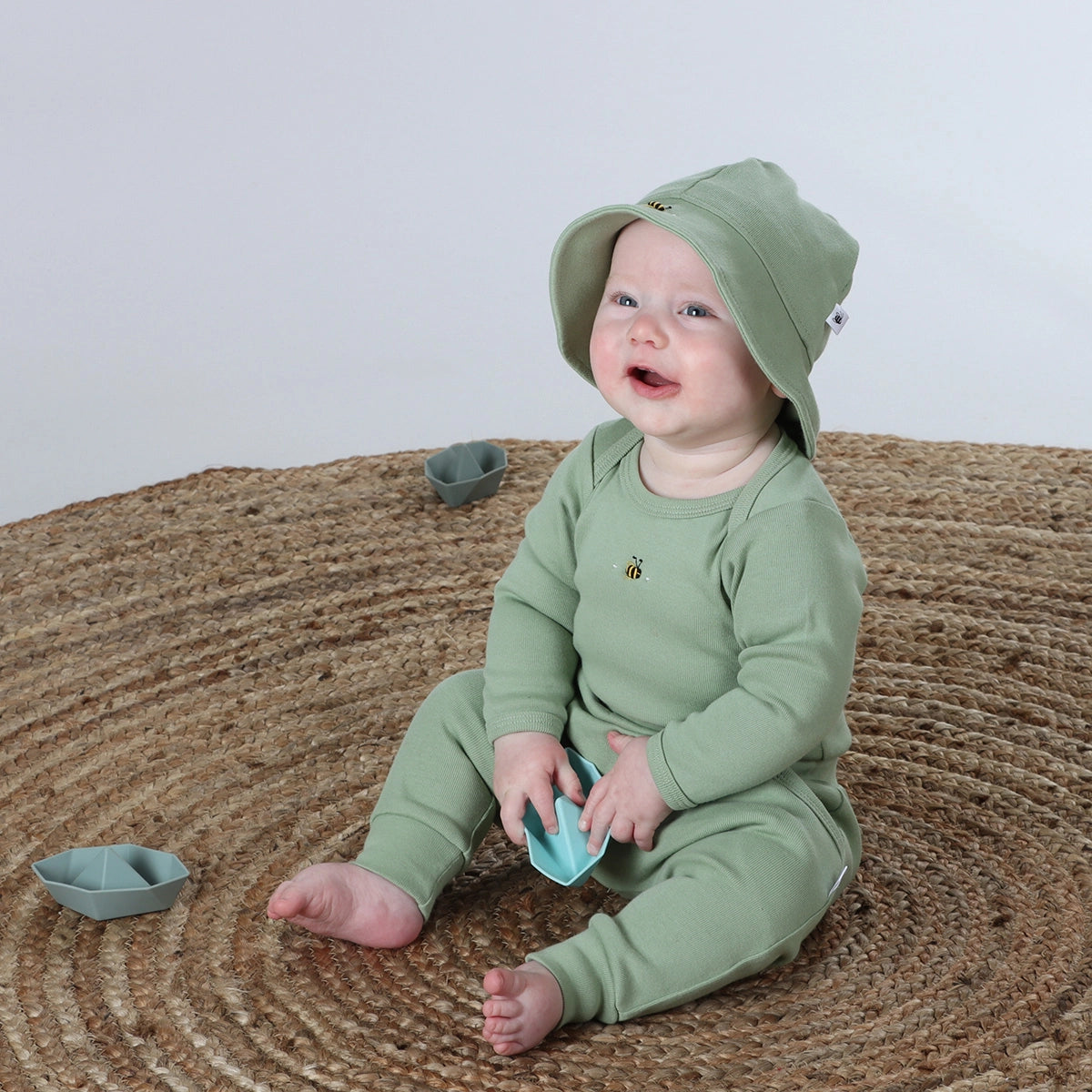 Baby in a green outfit sitting on a textured surface with a plain background