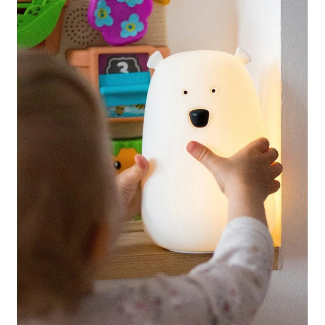 A child's hand touches a glowing white polar bear-shaped night light on a wooden shelf in a nursery setting.