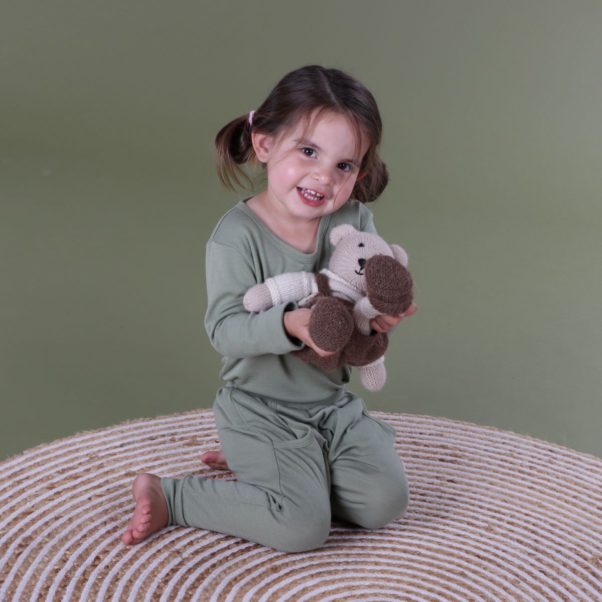 Girl wearing Arctic Adventure Merino Long sleeve top in Moss from Dimples New Zealand holding a toy