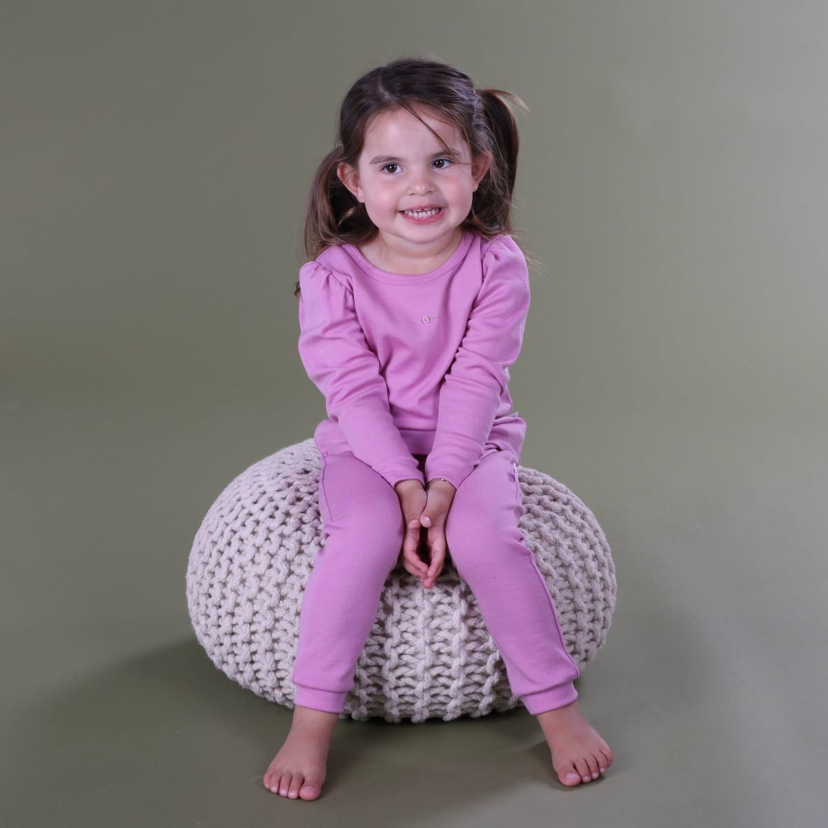 Baby firl sitting on pillow wearing merino puff sleeve top paiting it with leggings in orchid colour