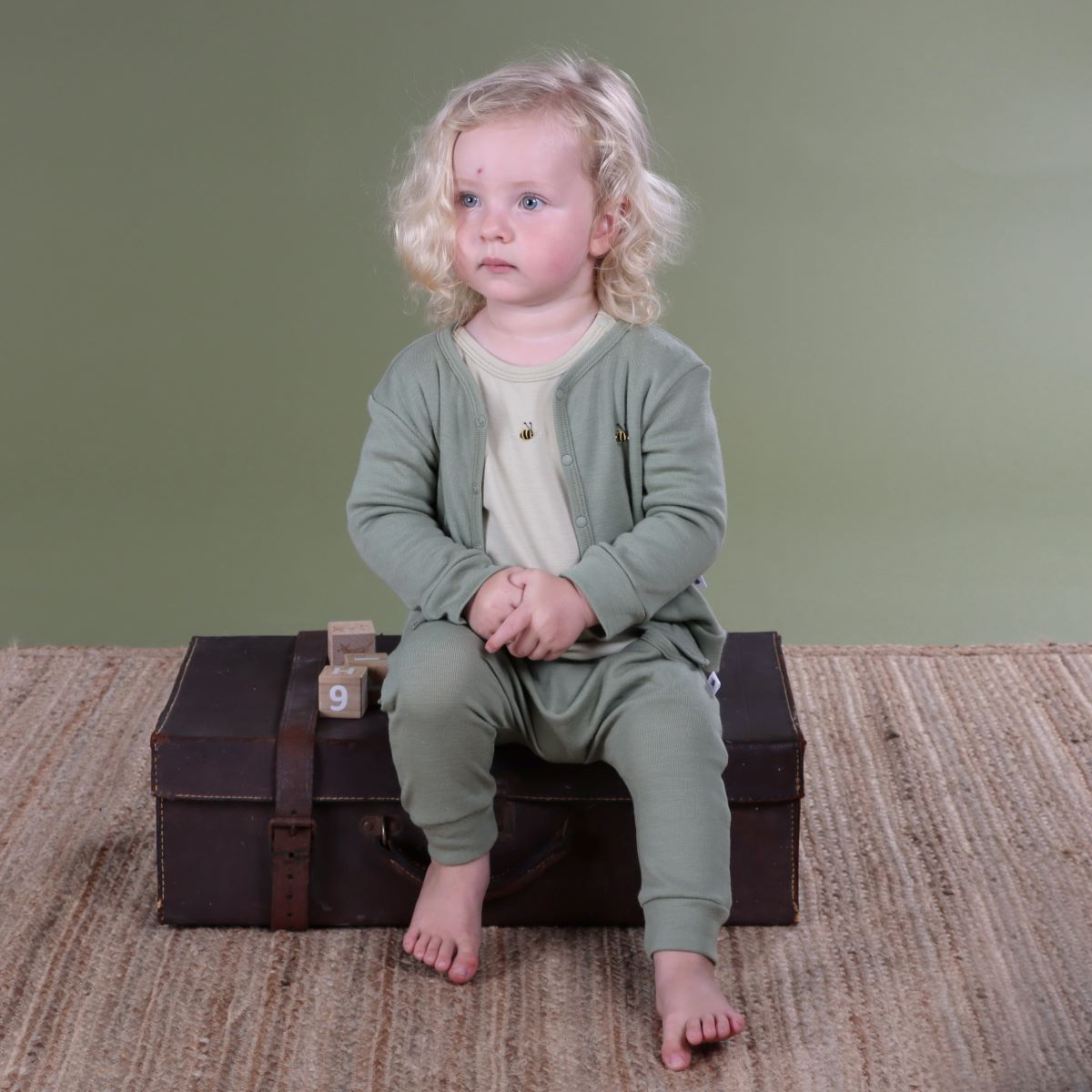 Baby wearing Merino Arctic Adventure 2ply Cardigan in Moss from Dimples sitting in a room