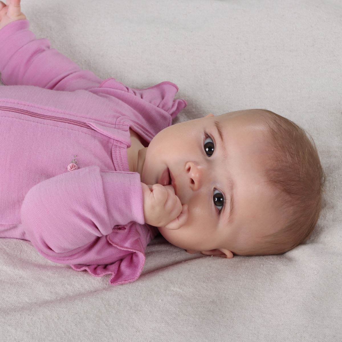 Closeup image of Baby girl sleeping wearing Orchid Merino Frill Zip Baby grow