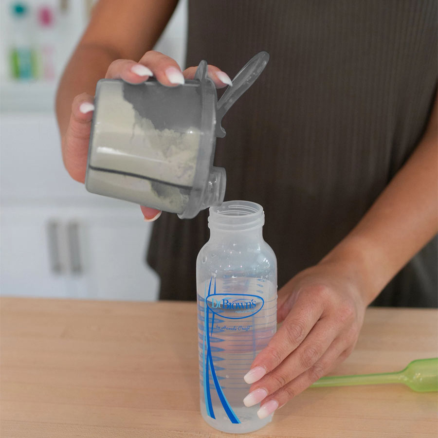 Lady adding Milk powder from dispenser into feeding bottle