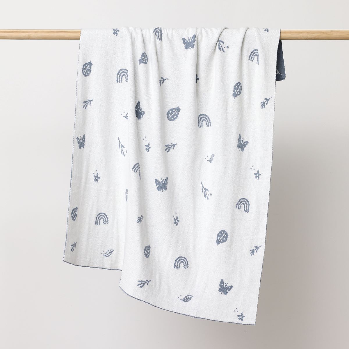 Reversed white coloured blanket with butterflies, betelnuts, flowers and leavers printed in sky blue hanging on the wooden rod to display.