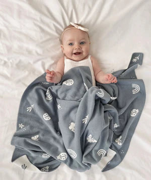 Smiling Baby sleeping on the bed covered with the Enchanted sky blue blanket printed with different elements.