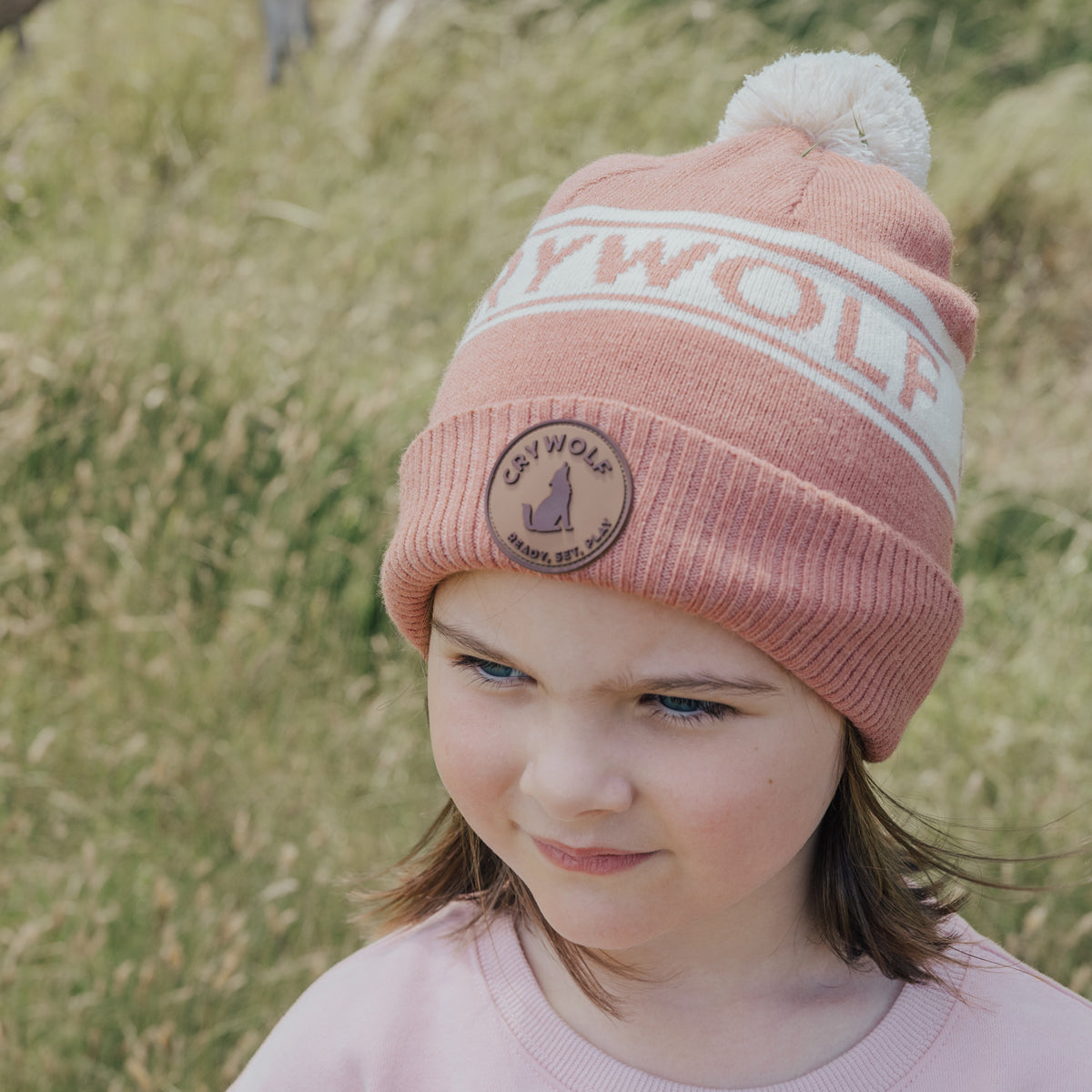 Girl wearing Rosewood Pom Pom Cotton Beanie with Cry Wolf logo standing in a farm