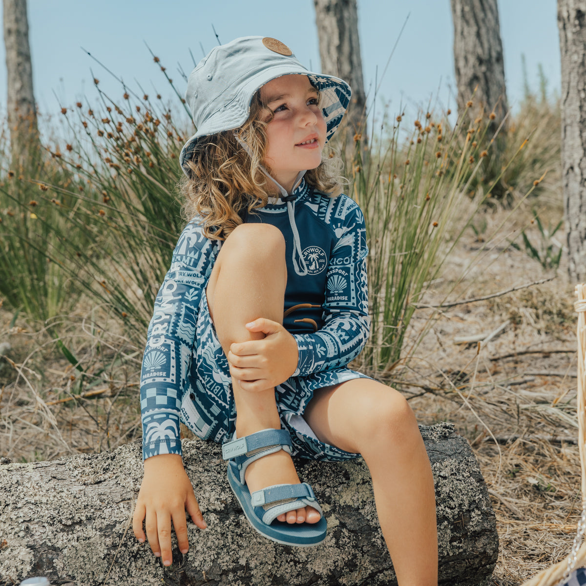 Child sitting on a rock while wearing Crywolf beach sandals in Seaside Blue