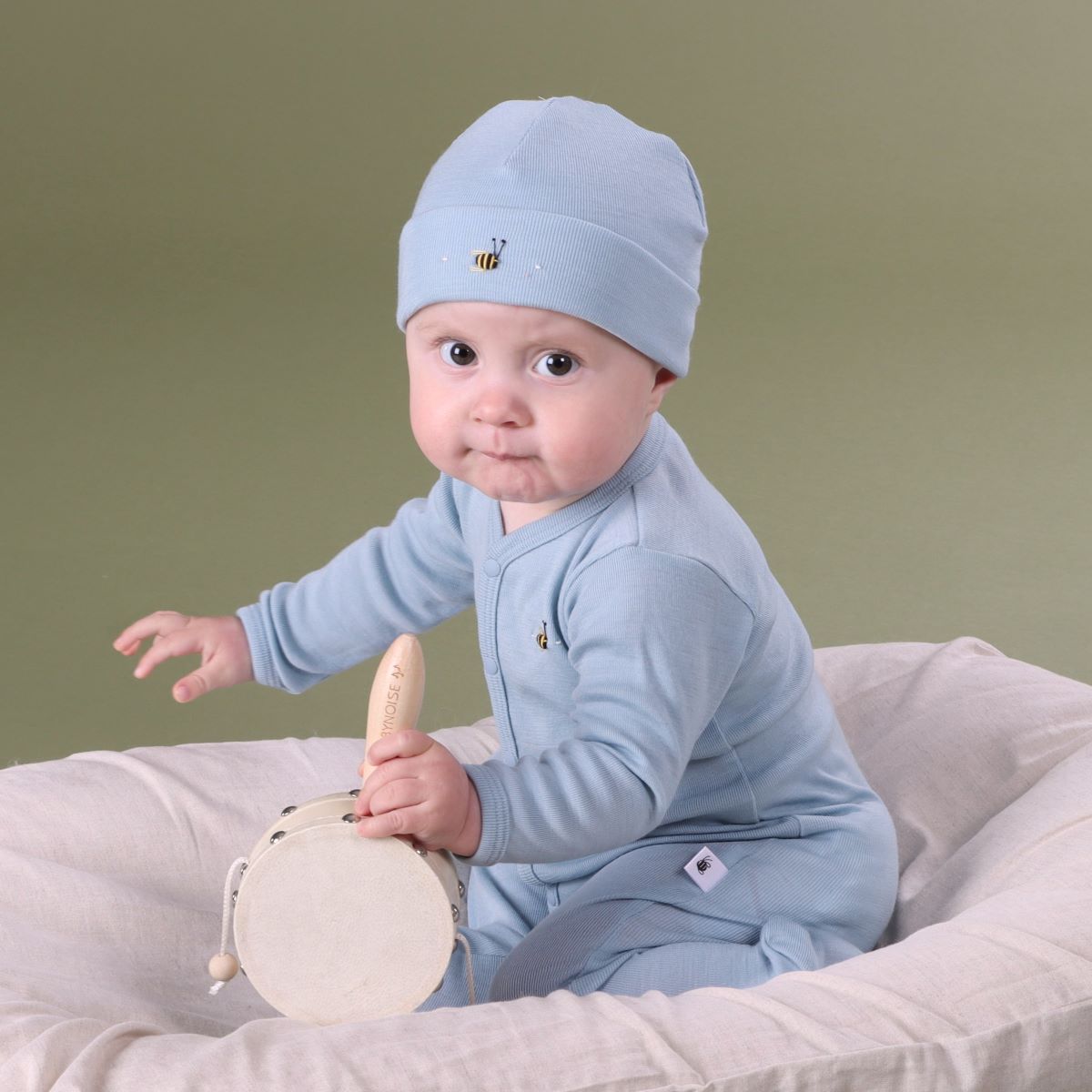 Baby playing in a lounger wearing Merino baby grow with buttons with bee embroidery pairing it with merino beanie