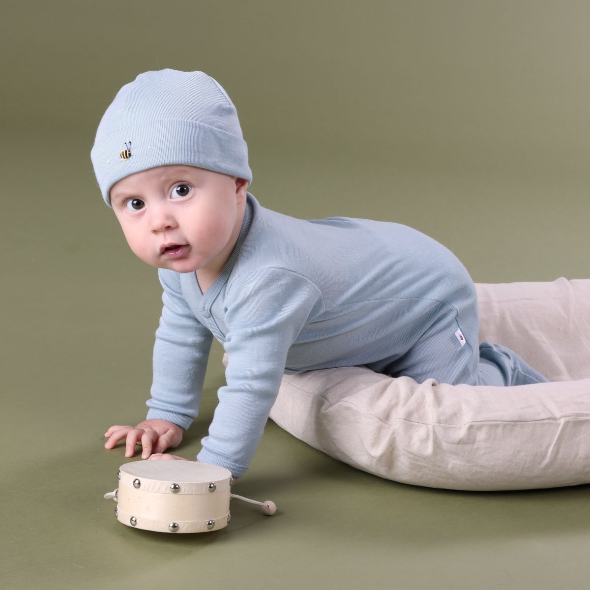Baby crawling outside lounger wearing Merino baby grow with buttons with bee embroidery pairing it with merino beanie