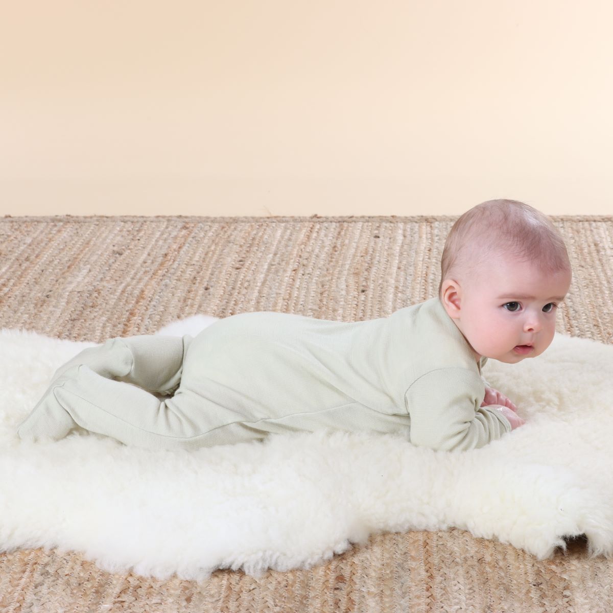 Baby playing on a rug wearing Cosy dreams Merino Baby grow in tea green bee from dimples new zealand 