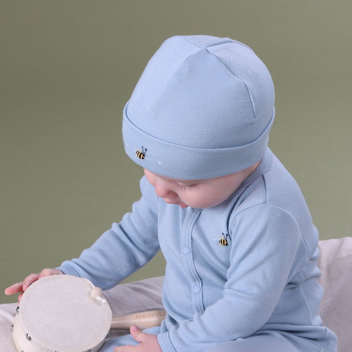 Baby playing wearing merino beanie and baby grow with bee embroidery
