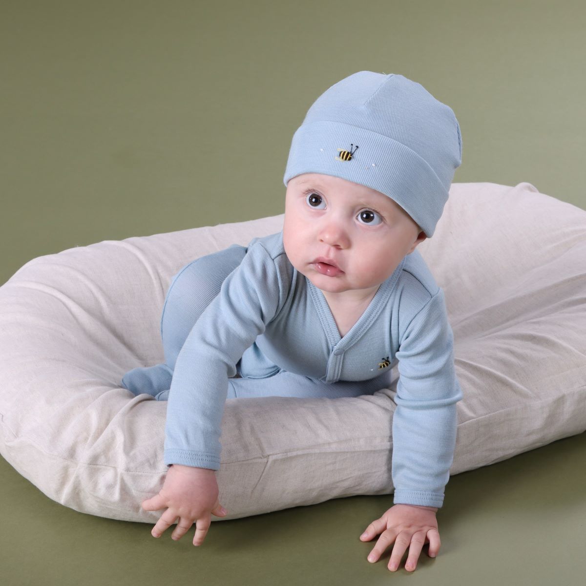 Baby in a lounger wearing merino beanie and baby grow with bee embroidery