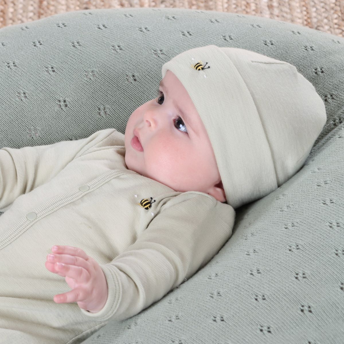 Baby wearing Cosy Dreams Merino Beanie in Tea Green from Dimples lying in a lounger