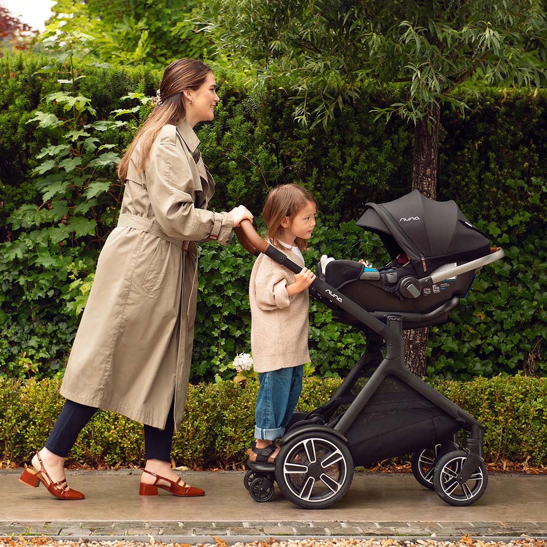 Baby riding with Nuna Demi Next Rider Board for stroller and mother holding her from back.
