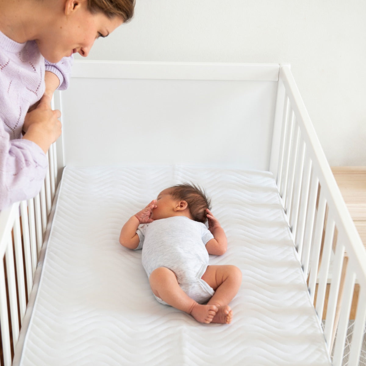 Mother lookin at a baby sleeping in a cot 