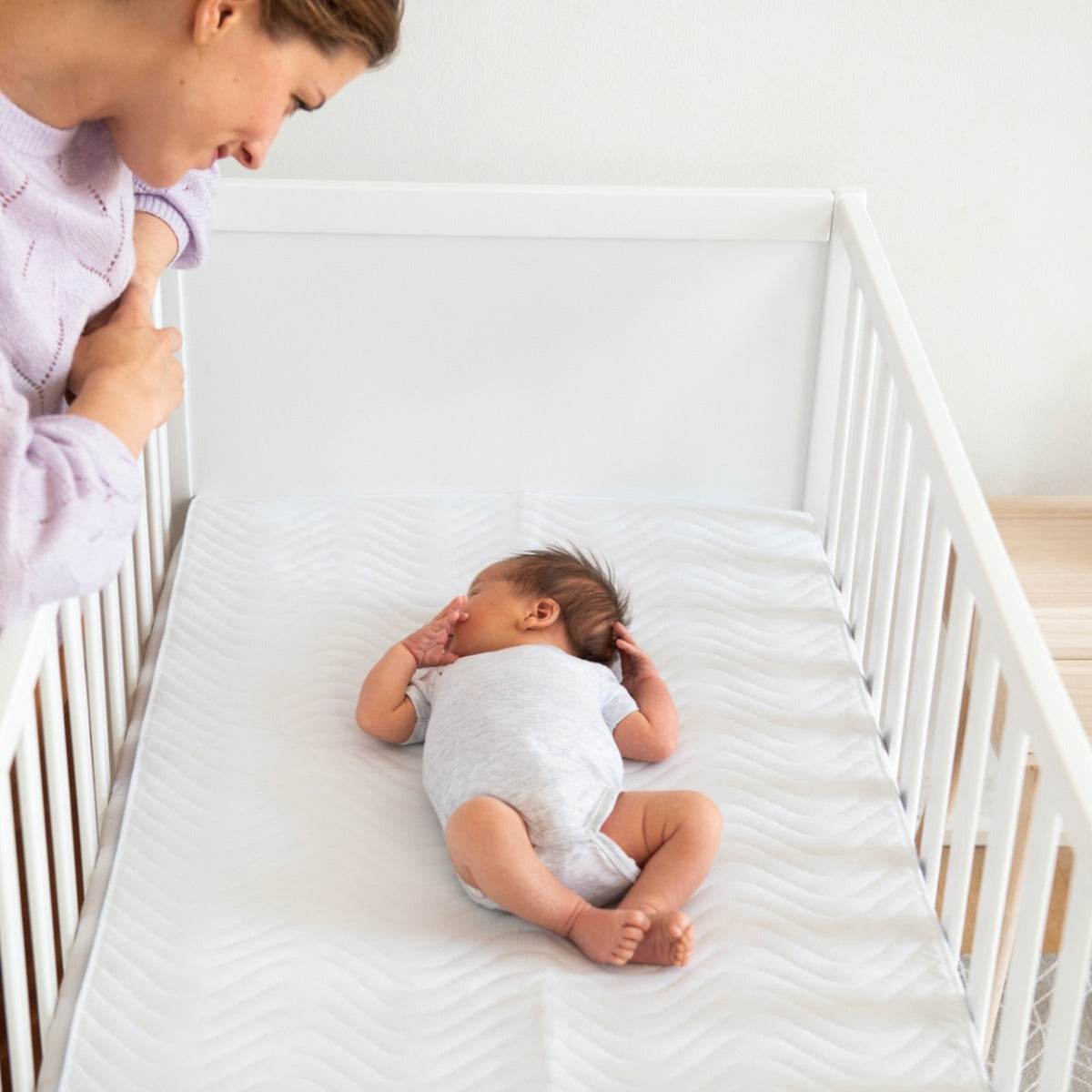 Mother lookin at a baby sleeping in a cot 