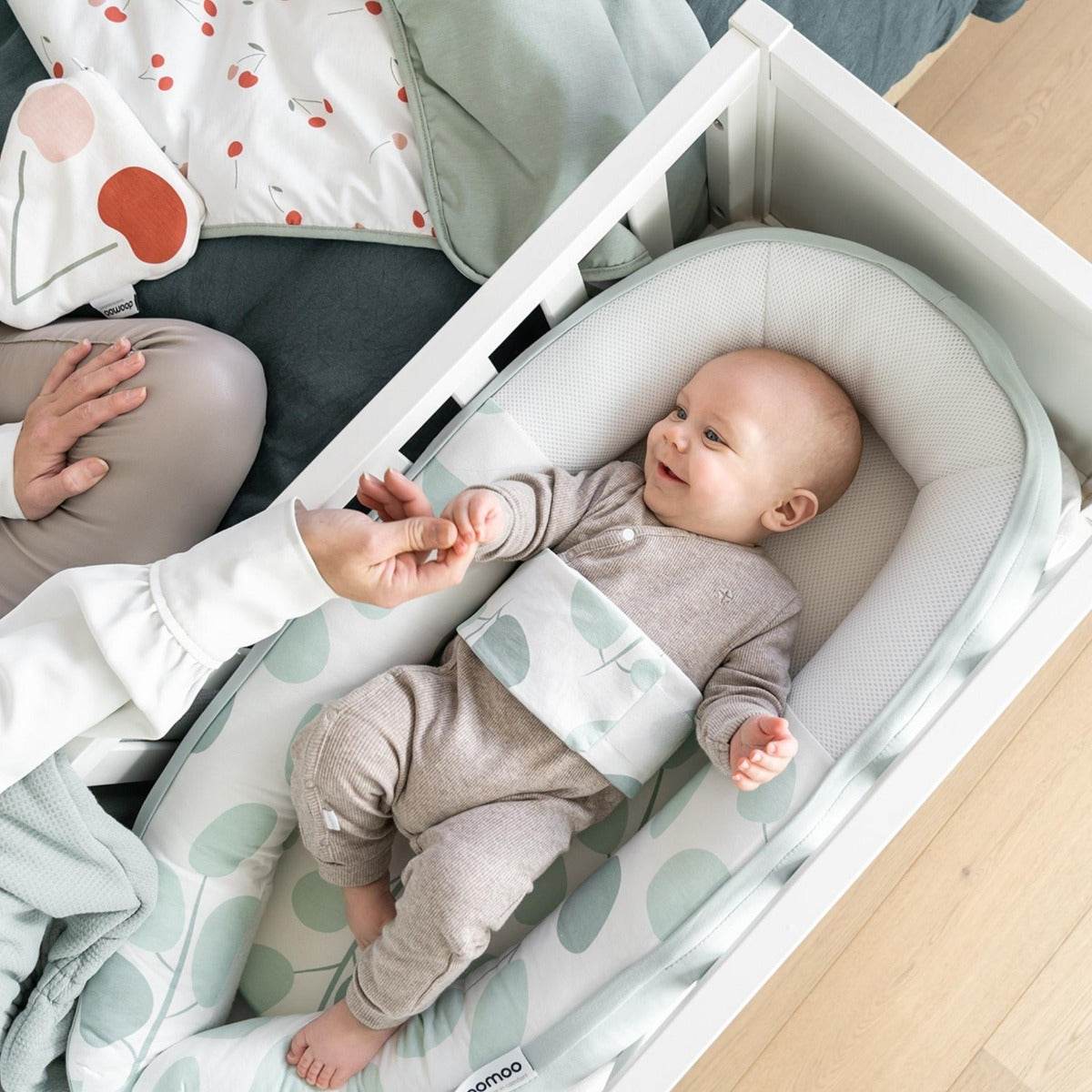 Baby in Doo Moo Cocoon nest in Leaves Aqua Green in bassinet 