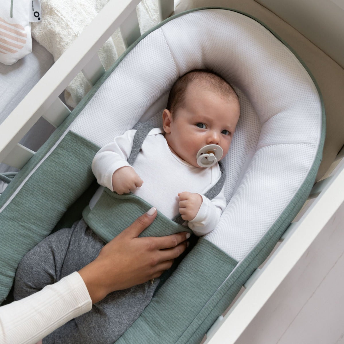 Baby laying in Doo Moo Cocoon nest in Tetra Jersey Green with mother's hand for comfort 