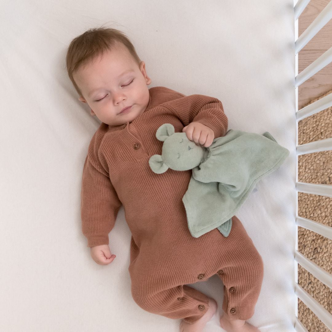 Baby sleeping peacefully in cot holding doomoo bunny detachable baby soother in sage green