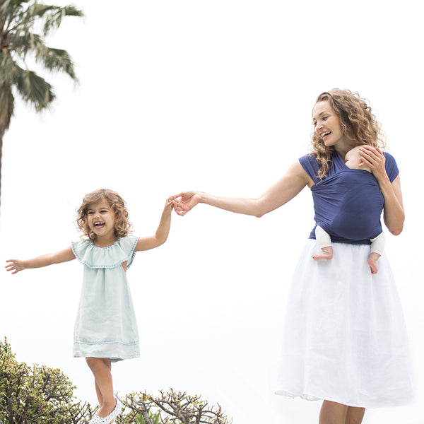 Mother holding baby in Ergobaby Indigo aura wrap and playing with another daughter