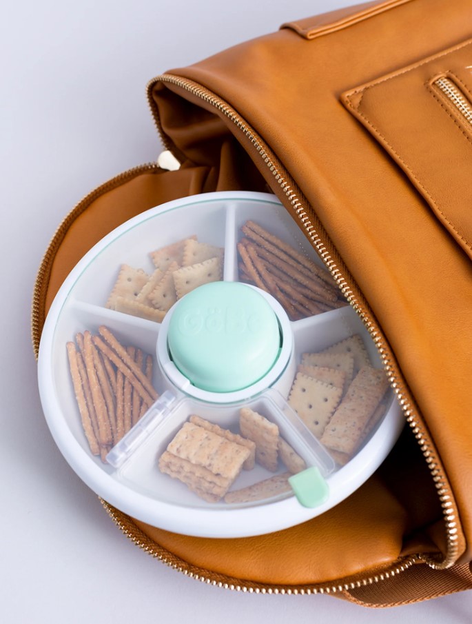 GoBee small snack spinner in teal and white example of it being fitting in a brown bag.
