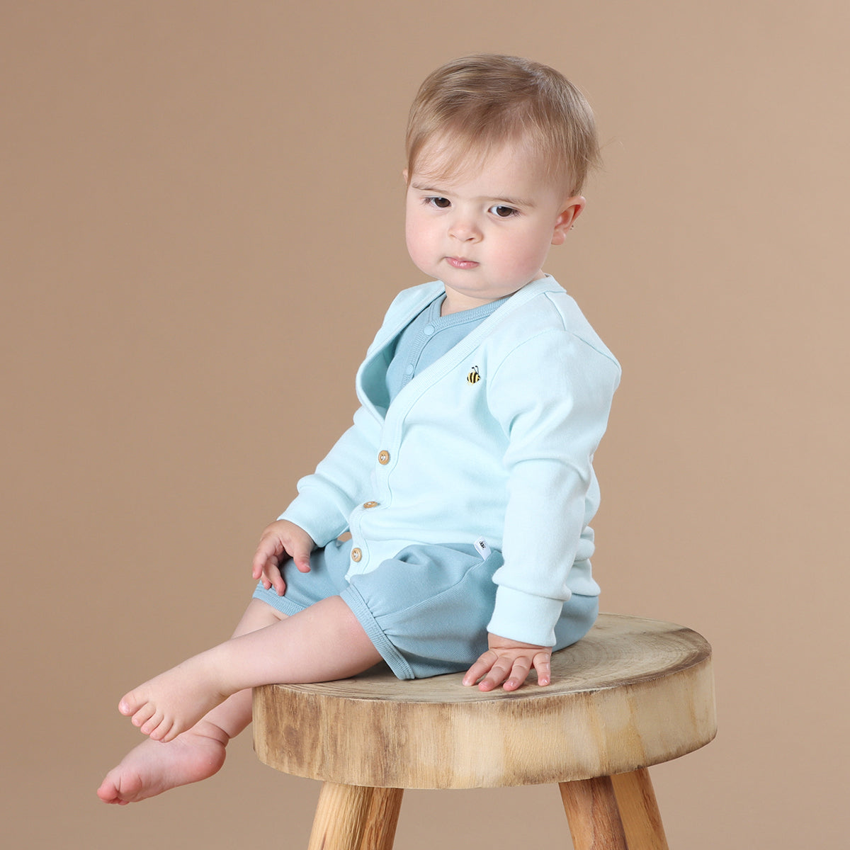 Baby sitting on a stool while wearing Dimples summer 2022/23 collection pastel skies cotton cardigan in Blue