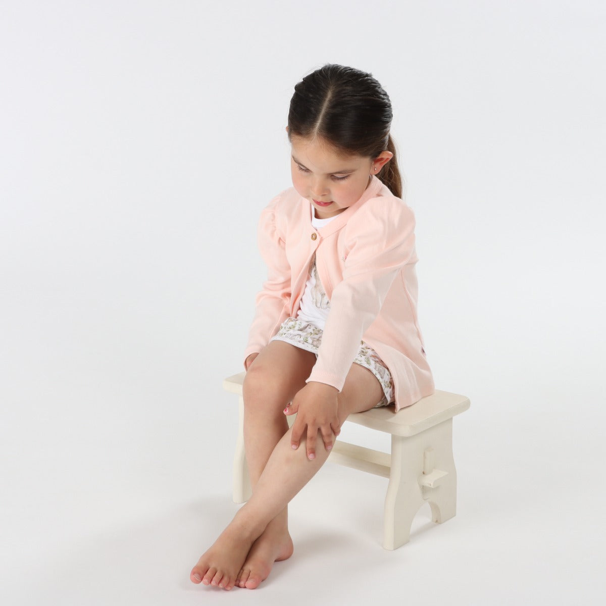 little girl sitting on a stool while wearing Dimples Pastel Skies Cotton Puff Cardigan  in Pink