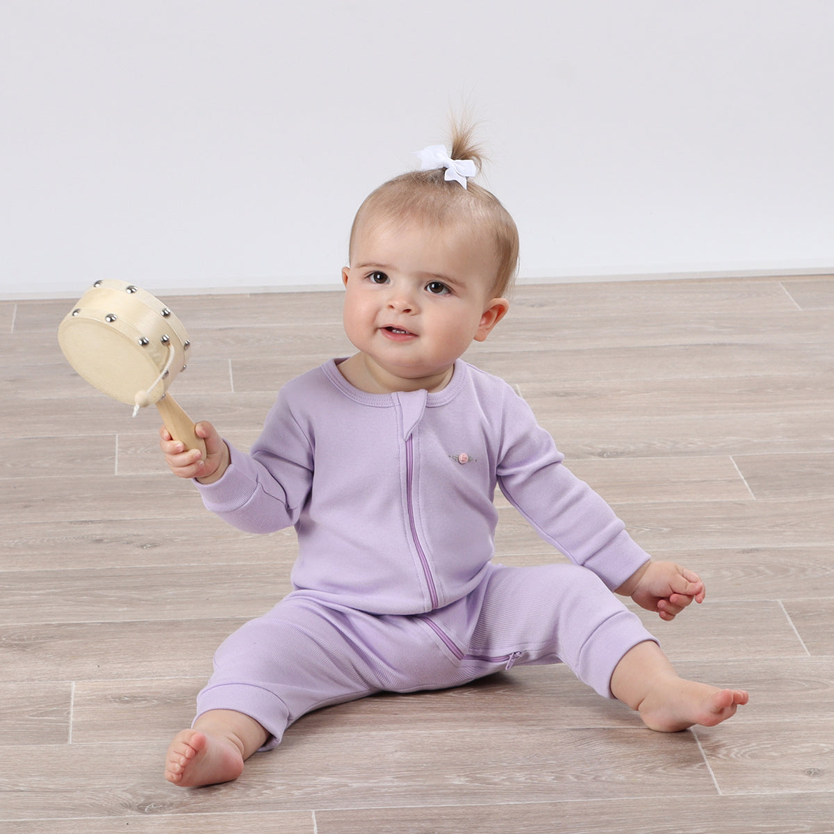 Cute baby girl wearing Cotton Zip lilac Babygrow with rose embroidery and playing