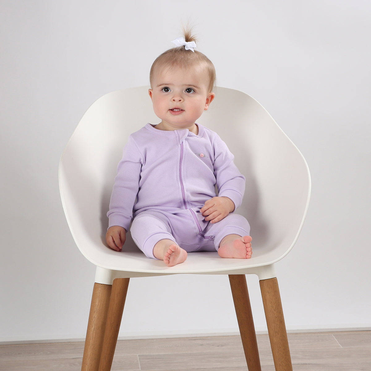 Cute baby girl sitting on chair wearing Cotton Zip lilac Babygrow with rose embroidery