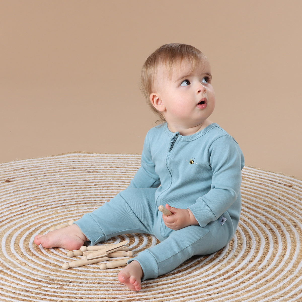 Little girl looking behind wearing Cotton Zip long sleeve Babygrow with bee embroidery in ocean color
