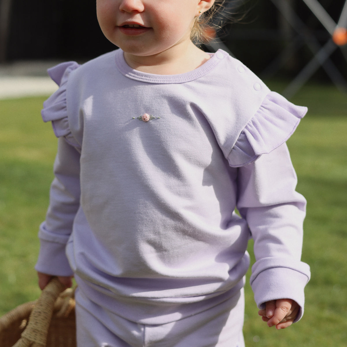 Little girl outside wearing Cotton Frill Jumper in lilac with rose embroidery