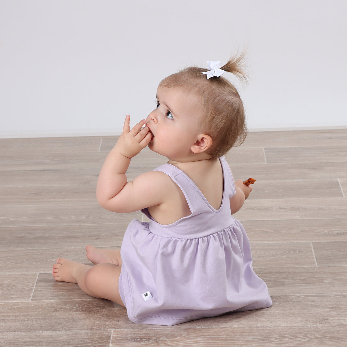 Playful baby girl wearing Cotton Pinafore dress for girls in lilac with rose embroidery and fliss and frankie ribbon bow hair clip