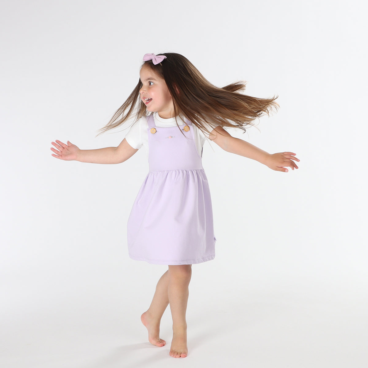 Playful baby girl wearing Cotton Pinafore dress for girls in lilac with rose embroidery and fliss and frankie bow headband