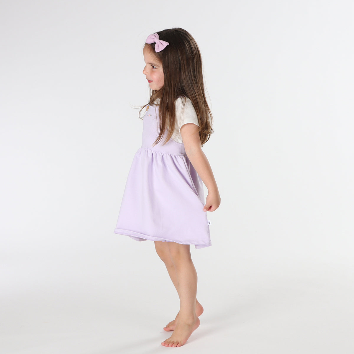 Playful baby girl wearing Cotton Pinafore dress for girls in lilac with rose embroidery and fliss and frankie bow headband