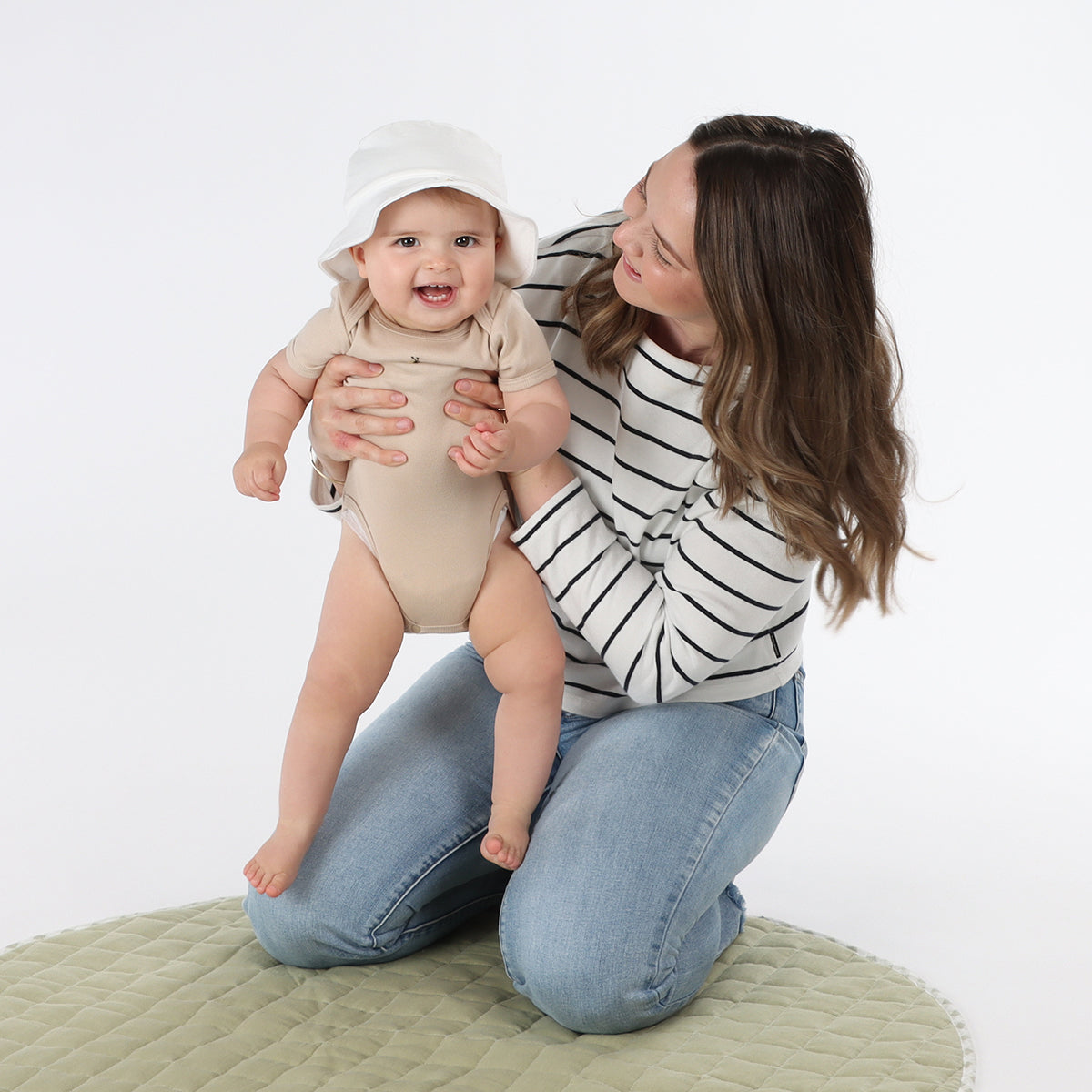 Mother holding baby wearing Dimples bodysuit from the Dimples 2024 Fashion Collection in Sand