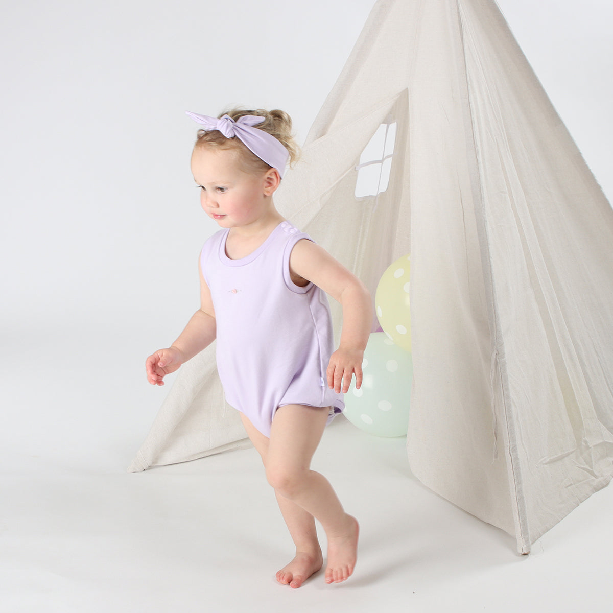 Baby playing wearing Cotton Slouch Bodysuit in lilac with rose embroidery and cotton headband