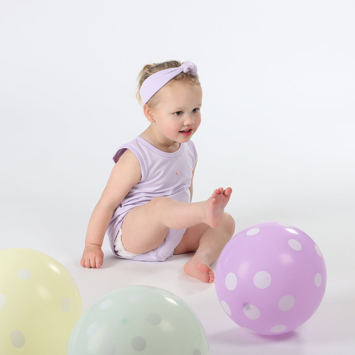 Baby playing wearing Cotton Slouch Bodysuit in lilac with rose embroidery with cotton headband