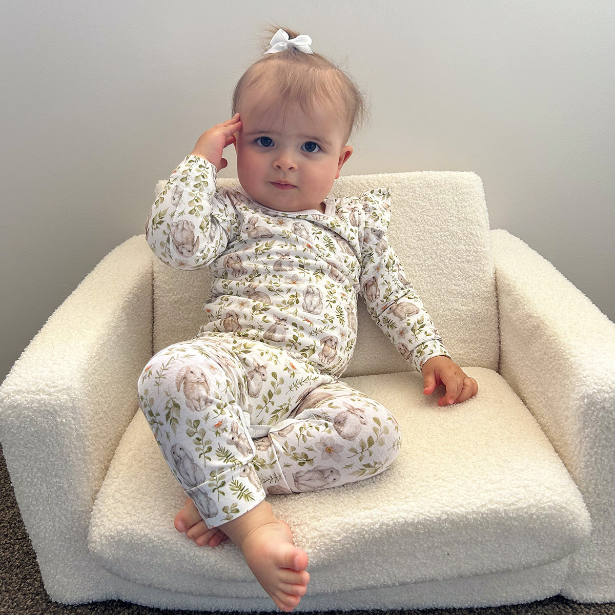 Baby girl sitting on soft chair wearing Little bee by Dimples Cotton Frill Babygrow with bunny print