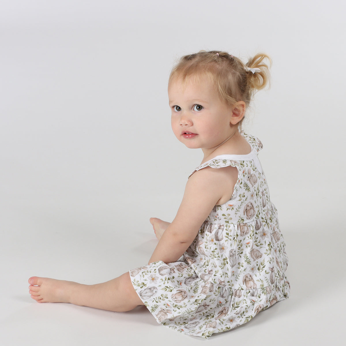 Little girl sitting down, wearing Little bee cotton tiered dress in white with bunny print 